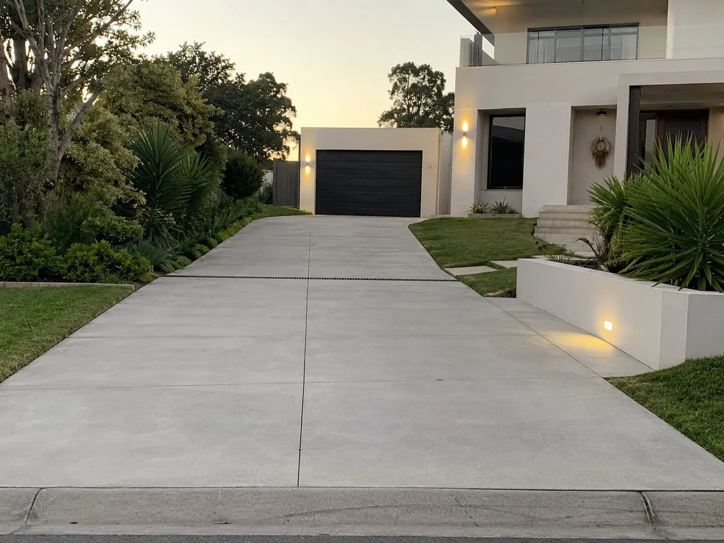 Repaired concrete driveway with clean saw-cut joints leading to a lit garage at dusk