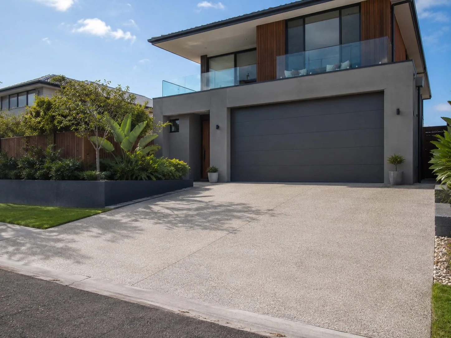 Freshly sealed exposed aggregate driveway with a soft sheen in front of a dark double garage