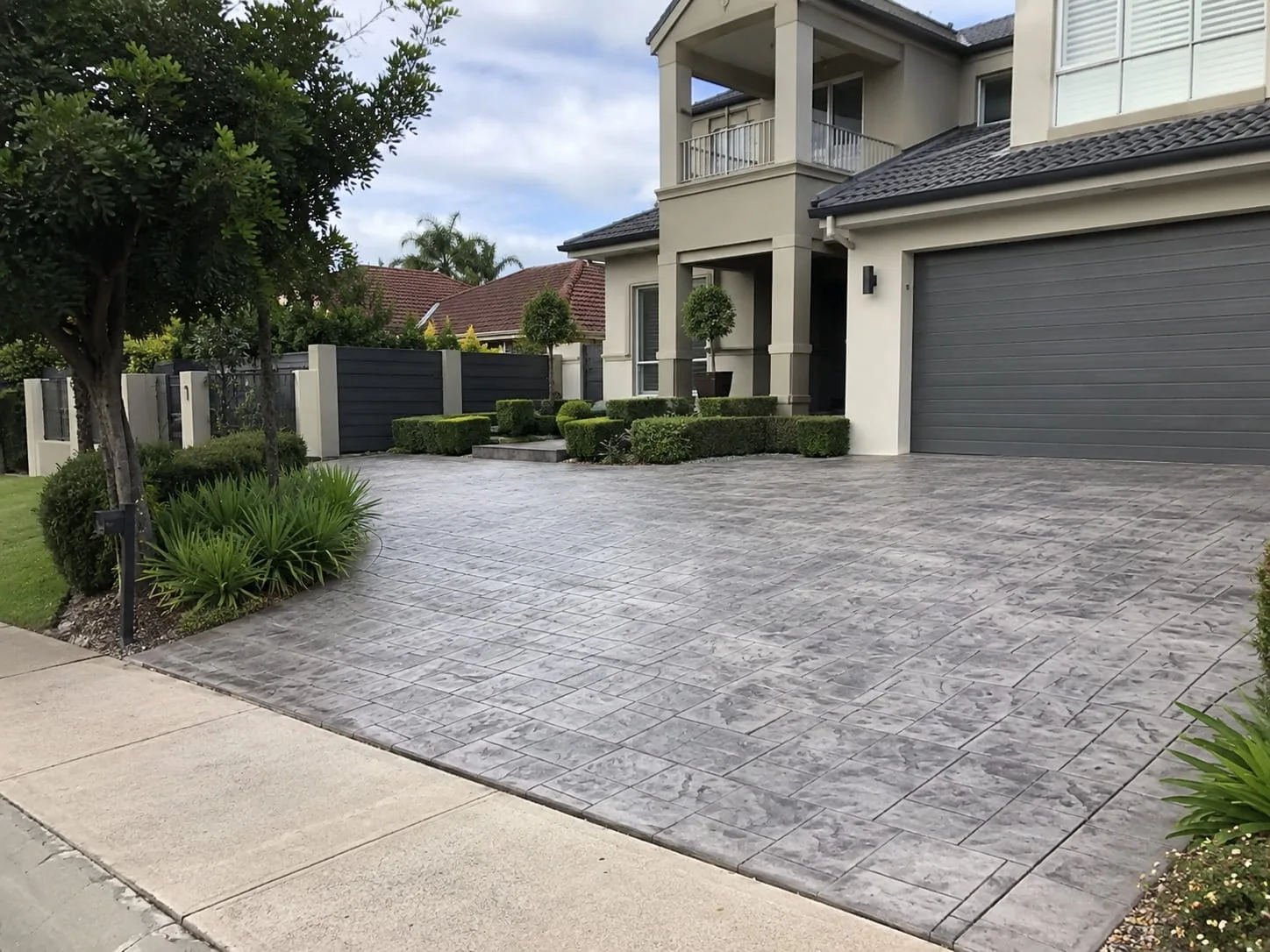 Grey slate-pattern stamped concrete driveway framed by clipped hedging and a street tree